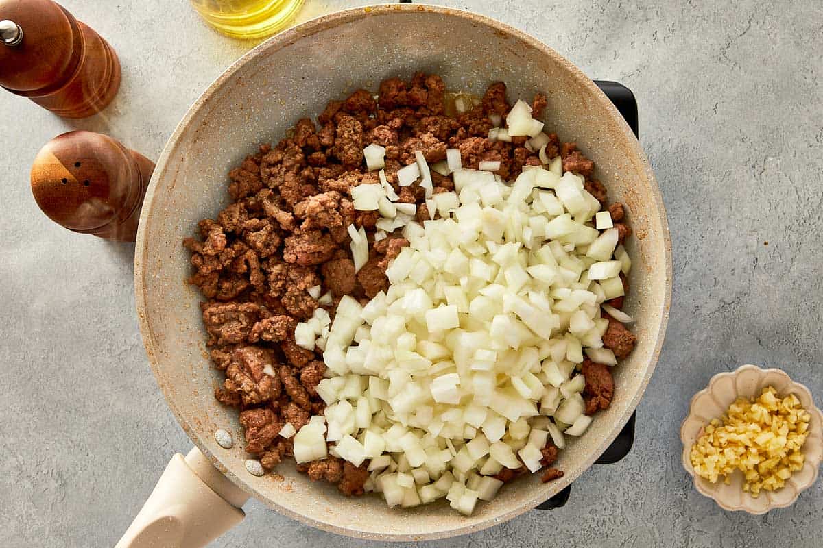 top overview of garlic, onion and beef in a beige pan