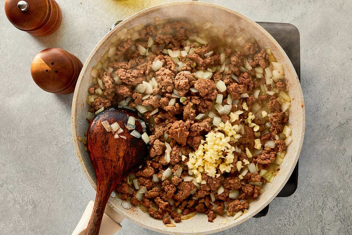 top overview of garlic, onion and beef being mixed in a beige pan