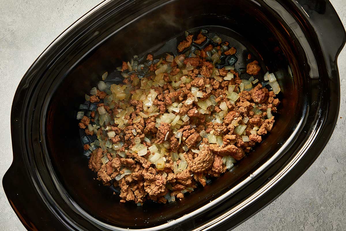 top overview of garlic, onion, vegetables and beef being cooked in the slowcooker