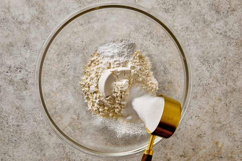 Mixing dry ingredients for blueberry chocolate chip pancakes in a glass bowl, including flour, baking powder, baking soda, and sugar before adding wet ingredients.