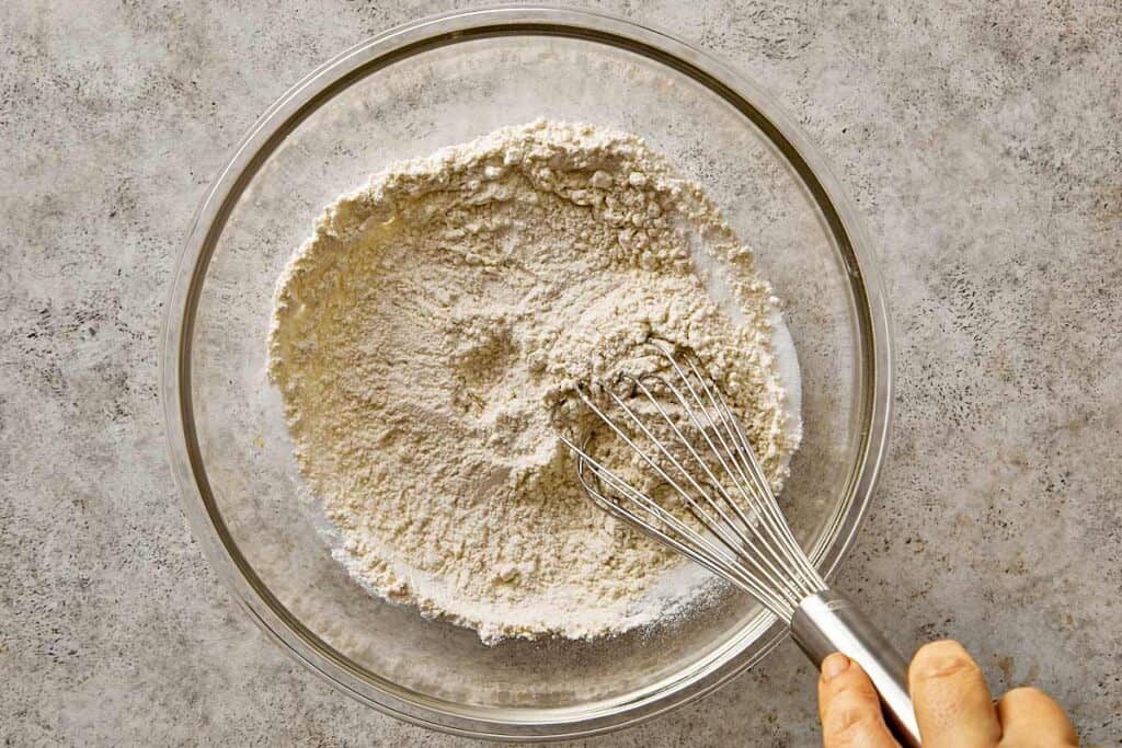 Whisking dry ingredients in a glass bowl to prepare blueberry chocolate chip pancake batter, combining flour, baking powder, baking soda, and sweetener.