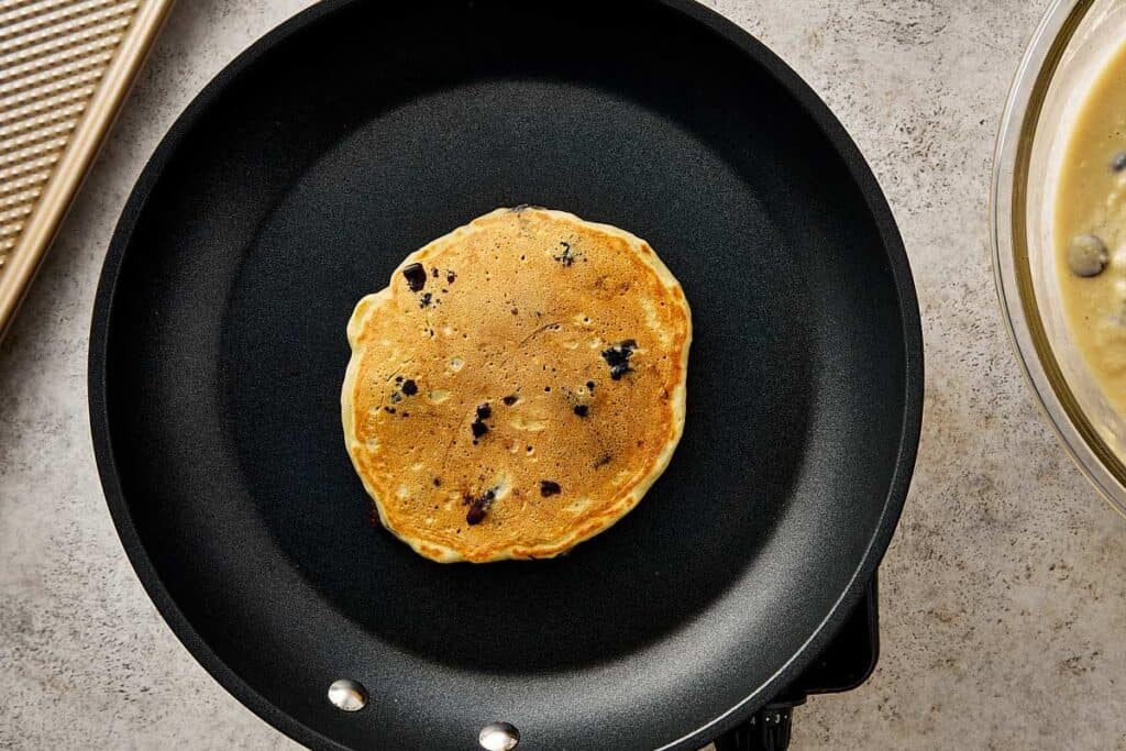 Flipped blueberry chocolate chip pancake cooking on a nonstick skillet, showing a golden brown surface with melted chocolate chips.