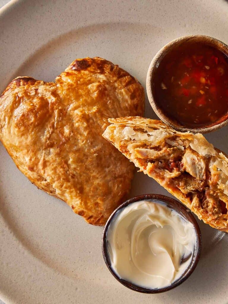 A top down view of a heart shaped tart and a half hart tart sliced in 2 with marry me chicken stuffing inside. A tomato sauce relish in a jar on the side.