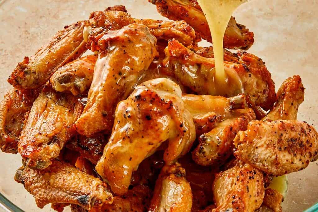 Pouring lemon pepper butter sauce over crispy chicken wings, coating them evenly before serving