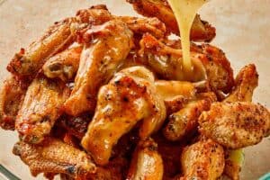 Pouring lemon pepper butter sauce over crispy chicken wings, coating them evenly before serving
