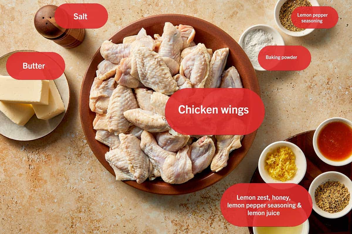 Crispy lemon pepper chicken wings ingredients including raw chicken wings, butter, lemon pepper seasoning, baking powder, salt, lemon zest, honey, and lemon juice laid out on a table