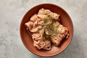 Seasoned ground chicken in a bowl with Italian seasoning, salt and spices