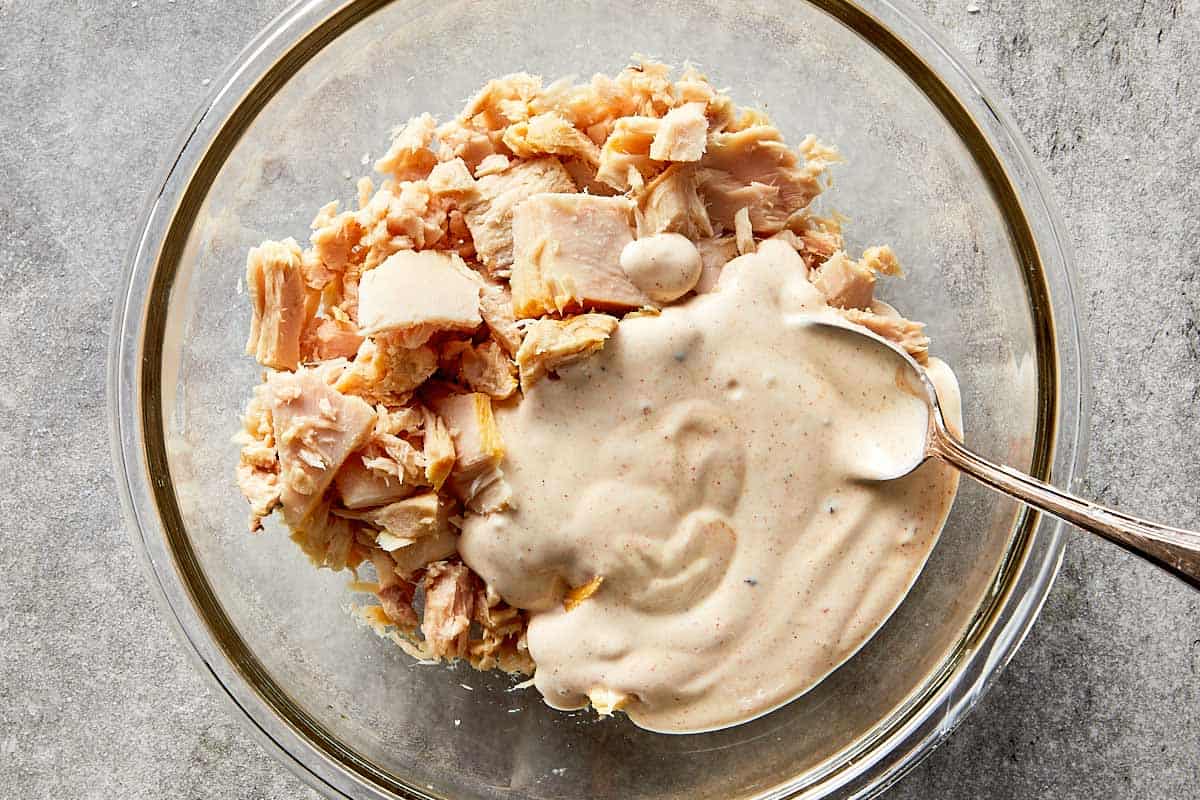 canned tuna added to creamy dressing in a mixing bowl