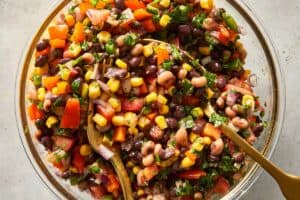 Black eyed pea salad tossed with lime vinaigrette, black beans, corn, tomatoes, peppers and fresh herbs in a large glass bowl.