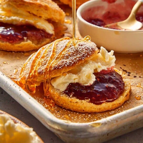 Buttermilk biscuits filled with jam and whipped cream, being drizzle with honey and sugar | CafeDelites.com