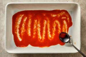 tomato sauce spread on the bottom of a baking dish before layering cabbage lasagna.