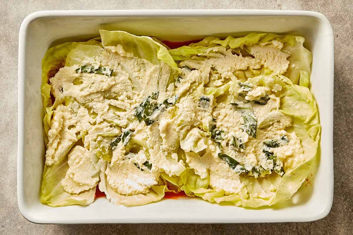 Cabbage leaves layered over tomato sauce in a baking dish while assembling cabbage lasagna.