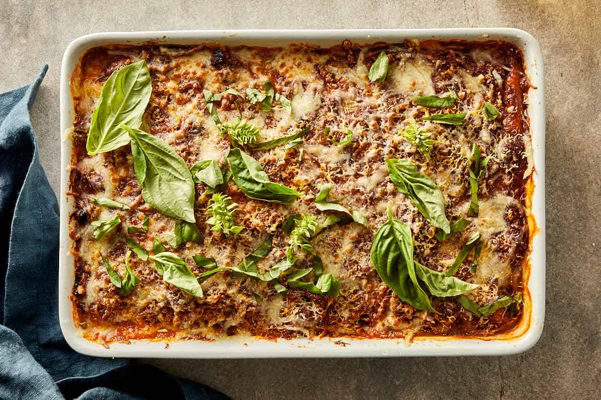 Baked cabbage lasagna topped with melted cheese and fresh basil in a baking dish.