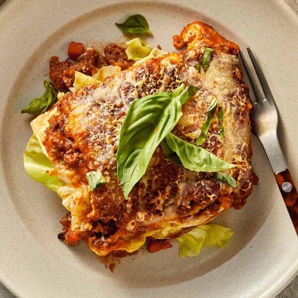 Slice of cabbage lasagna with ricotta, beef sauce, melted cheese, and fresh basil served on a plate.