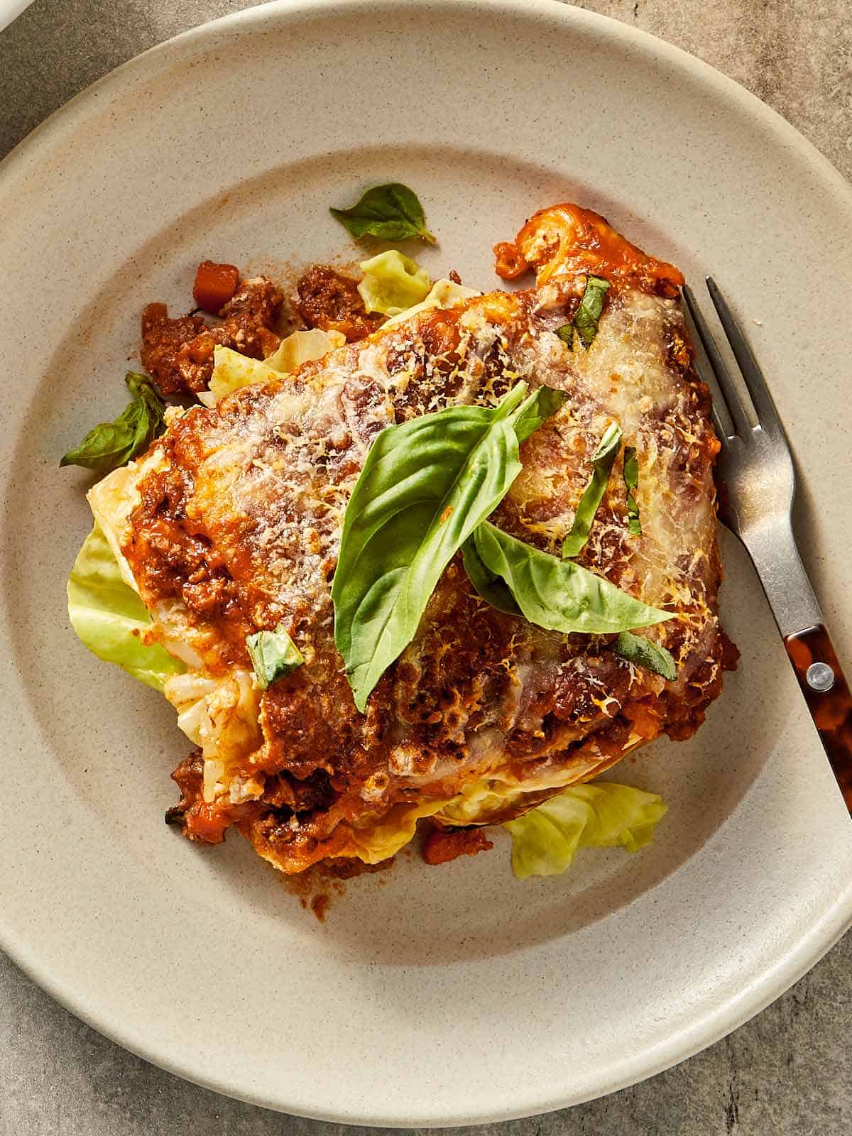 Slice of cabbage lasagna with ricotta, beef sauce, melted cheese, and fresh basil served on a plate.