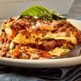 Slice of cabbage ricotta lasagna layered with beef meat sauce, melted mozzarella, ricotta filling, and tender cabbage leaves on a white plate with fresh basil on top.