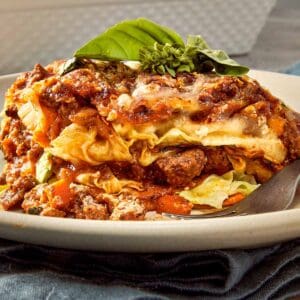 Slice of cabbage ricotta lasagna layered with beef meat sauce, melted mozzarella, ricotta filling, and tender cabbage leaves on a white plate with fresh basil on top.