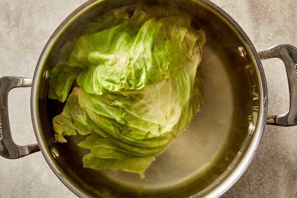 Whole green cabbage boiling in a large pot of salted water to soften the leaves for cabbage lasagna.