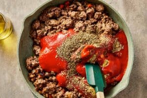 Passata, tomato paste, and dried herbs added to ground beef for cabbage lasagna sauce.