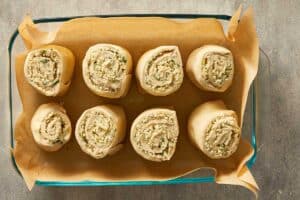Unbaked cheesy garlic rolls arranged in a parchment-lined baking dish