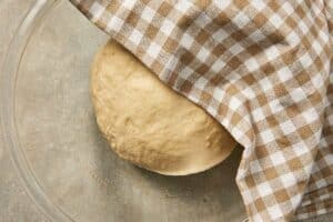 Garlic roll dough rising in a greased bowl covered with a kitchen towel