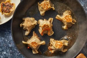 Dumplings frying in a skillet with the meat side flipped down, getting a savory crust.
