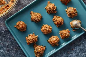 Small, even scoops of meat filling arranged on a blue baking tray.