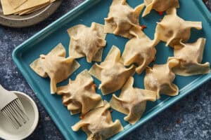 Dumpling meatballs covered with square wonton wrappers on a blue tray.