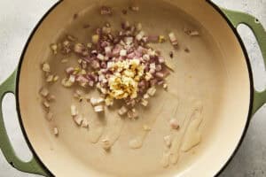 Chopped shallots and minced garlic sitting in a little olive oil inside a green pot before cooking