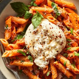 One-pot spicy vodka pasta made with penne, topped with a broken ball of fresh burrata, fresh basil leaves, grated cheese, and red chili flakes.