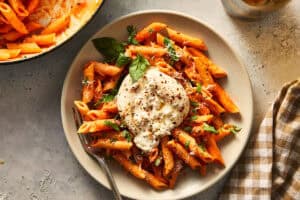 A single plated serving of spicy vodka penne pasta topped with a whole fresh burrata, fresh basil leaves, grated cheese, and red chili flakes.