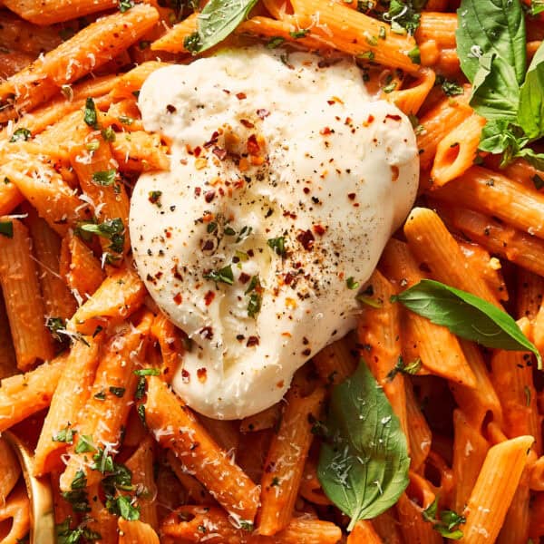 Close-up of one-pot spicy vodka pasta made with penne, topped with a broken ball of fresh burrata, fresh basil leaves, grated cheese, and red chili flakes.