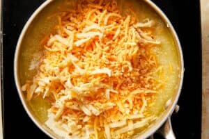 Chicken stock with grits, butter, heavy cream, cream cheese, and shredded cheeses at the top ready to mix