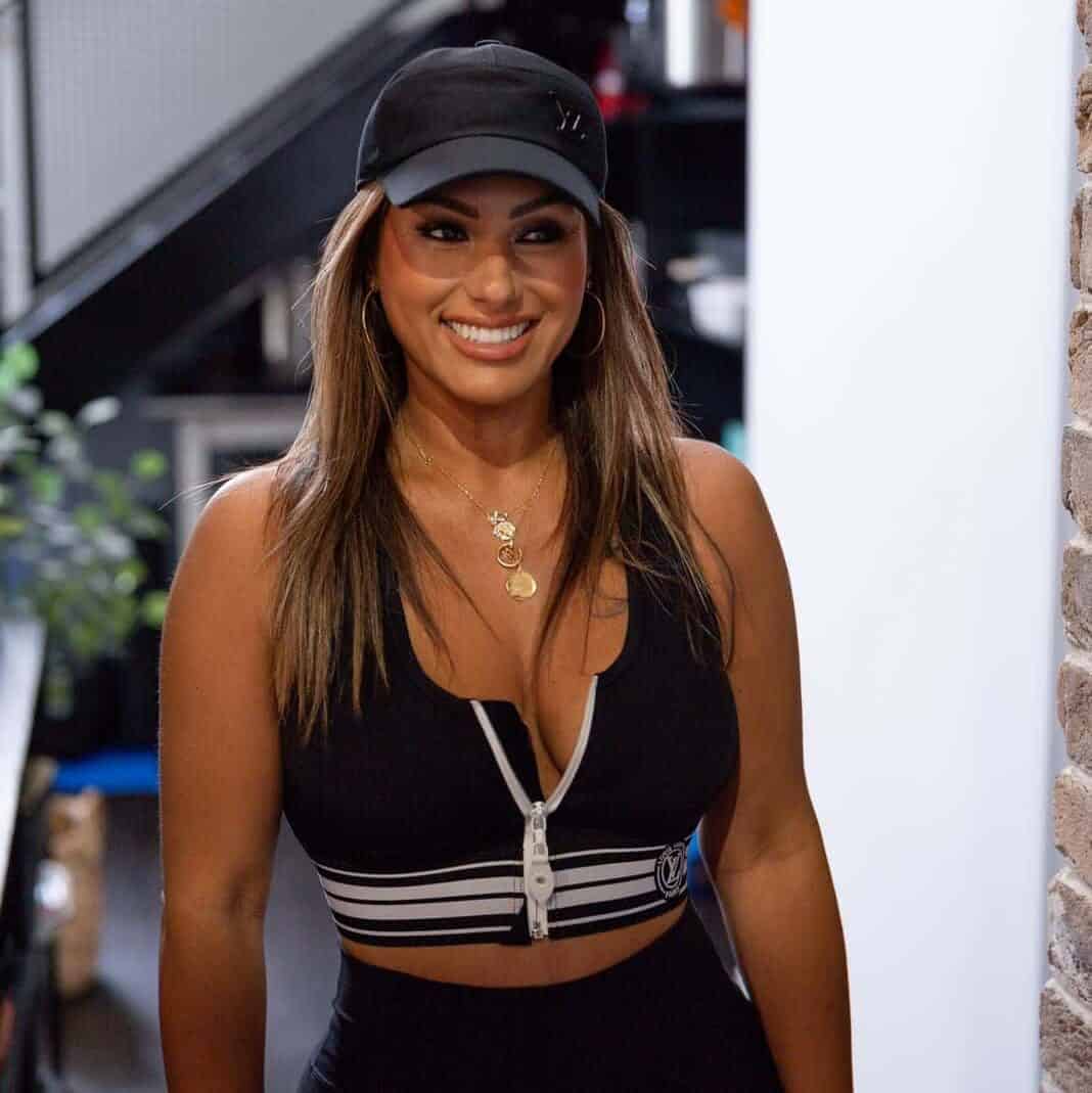 Karina smiling in a black athletic outfit and cap while standing indoors.