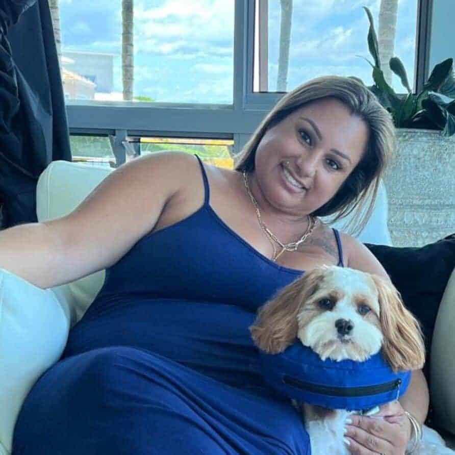 Karina smiling while sitting on a white couch with her small dog in her lap.