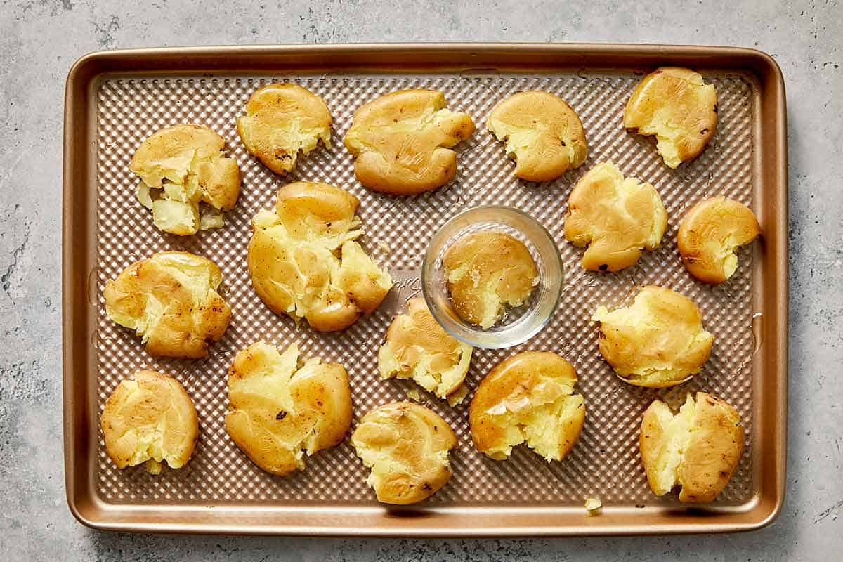glass flatting the potatoes in a baking sheet