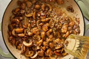 Pouring wine into the pan with chicken, mushrooms, and aromatics