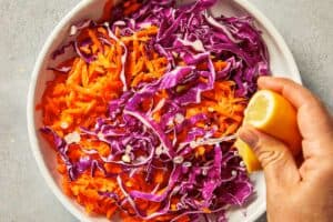 Squeezing lime juice over shredded red cabbage and carrots.