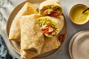 Finished shrimp burritos on a plate, one cut in half.