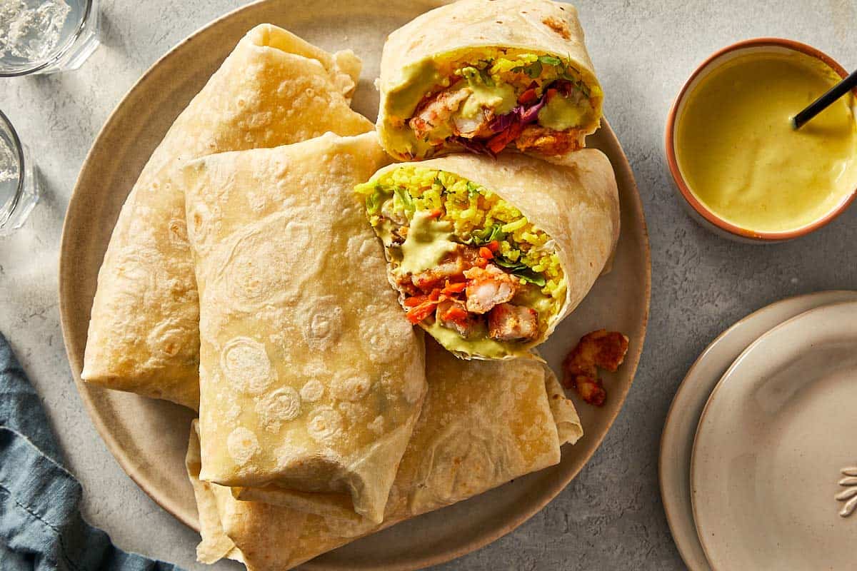 Finished shrimp burritos on a plate, one cut in half.