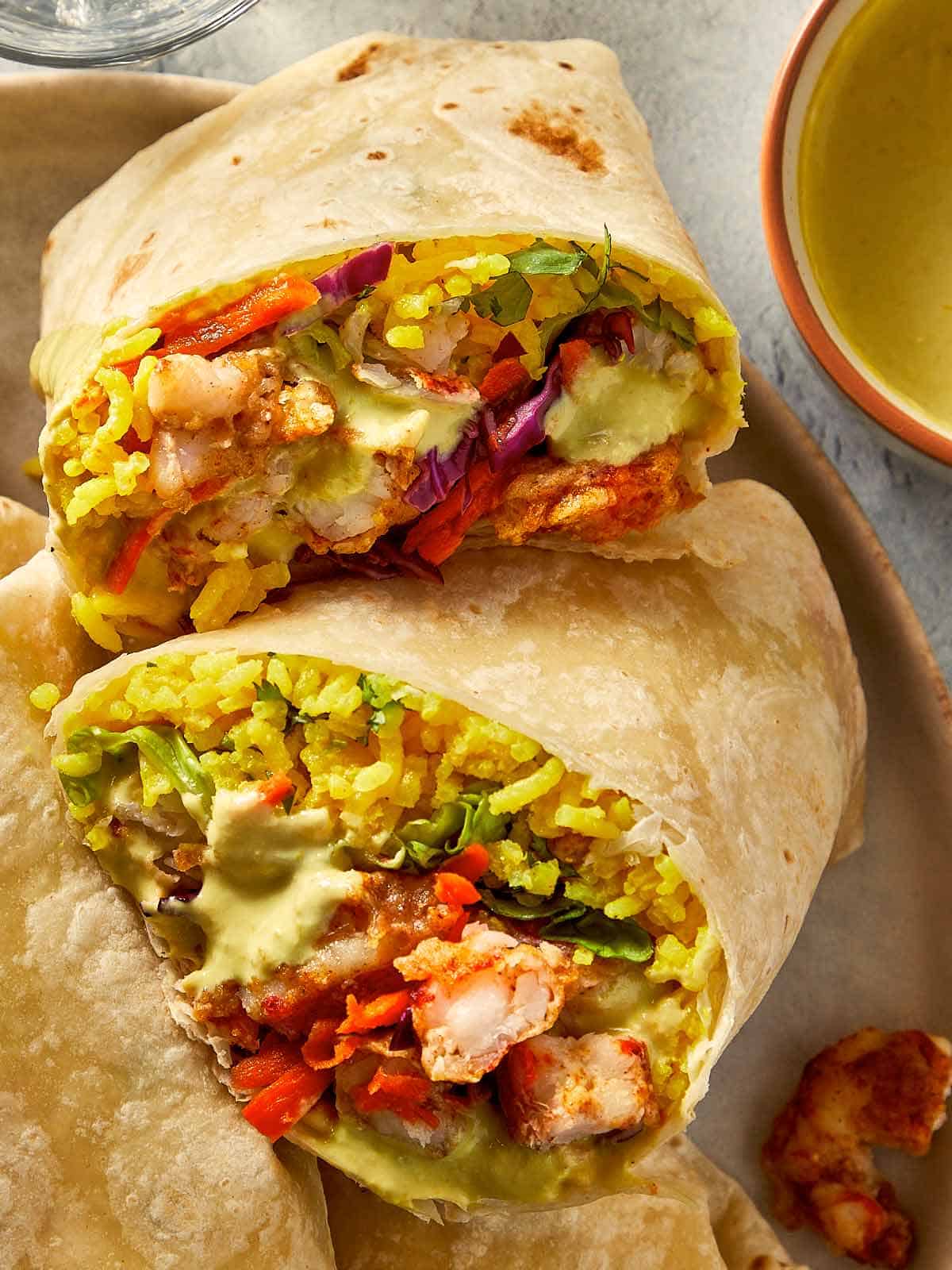 Finished shrimp burritos on a plate, one cut in half.