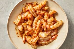 Raw shrimp being seasoned in a bowl