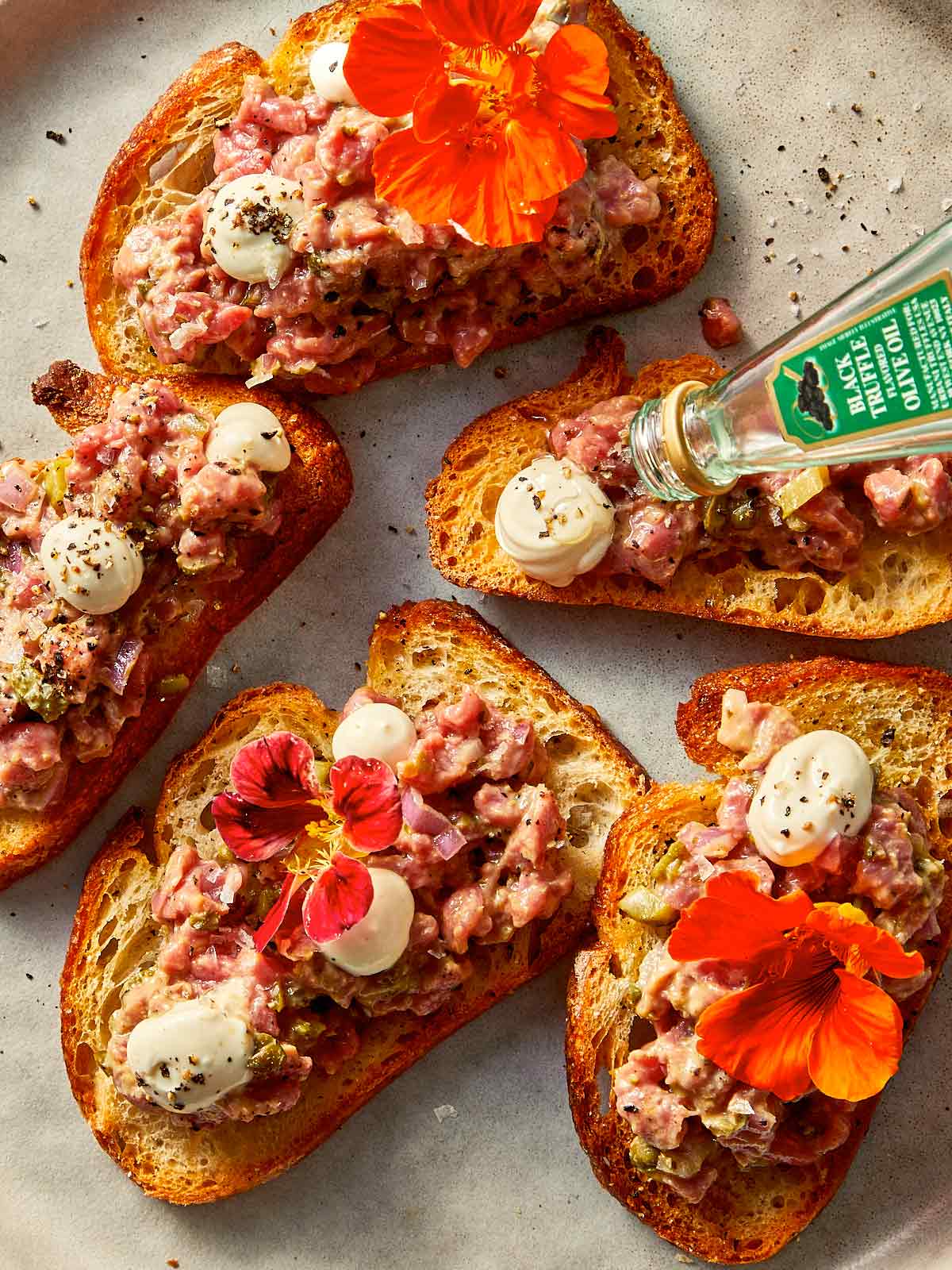 Toasts with Steak tartare at the top being drizzle with truffle oil