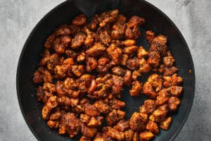 Seasoned diced chicken cooking in a black non-stick skillet.