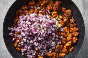 Finely chopped red onion and minced garlic added to the cooked chicken in the skillet.