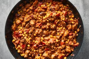 Thick chicken, corn, and tomato filling cooking in a skillet.