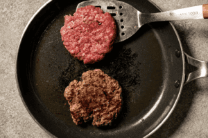 showing both parts of the beef patty in a pan. One being about to be flipped.